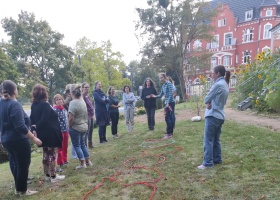 Zu sehen sind Mitarbeitende des Hospiz und des Kinderhospiz Schwerin in einem Workshop mit dem Titel Spiele für Groß und Klein. Sie stehen auf einer Wise und haben Seile in Ringen vor sich gelegt.