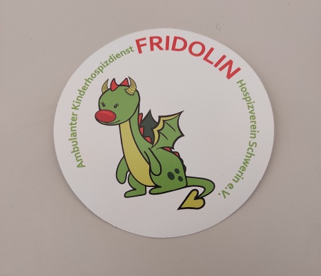 Das Hospiz Schwerin stellt vor: Der neue Name des Kinderhospiz in Schwerin heißt Fridolin. Das Logo zeigt einen freundlichen, grünen Drachen mit roter Nase, gelbem Bauch, niedlichen Flügeln und gekringeltem Schwanz. Der Name des Drachen lautet Fridolin.